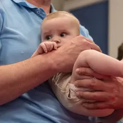 Niemowlę w ramionach mężczyzny, z odginaniem głowy do tyłu, patrzy zaciekawione.