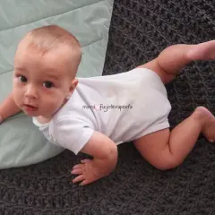 Małe dziecko na brzuchu, ćwiczy **piwoty kiedy** tylko może, na miękkim dywanie.