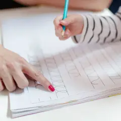 Dziecko ćwiczy grafomotorykę na kartach pracy, a dorosły pokazuje mu wzory do naśladowania.