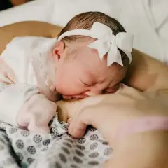 Słodki sen noworodka podczas karmienia. Maleństwo z białym memo na głowie przytula się do mamy.