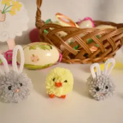 Urocze ozdoby wielkanocne zrób to sam dla dzieci: puchate króliczki i kurczaczek z pomponów, obok pisanki i koszyczek.