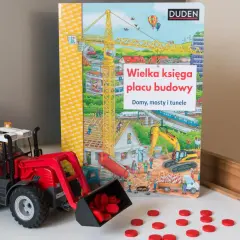 Czerwony traktor z ładowarką i rozsypanymi czerwonymi krążkami obok książki "Wielka księga placu budowy".
