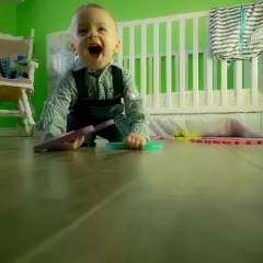 Chłopiec w ogrodniczkach bawi się na podłodze, zastanawiając się, ile czasu od pełzania do raczkowania.