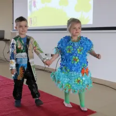 Chłopiec w eko stroju z opakowań po przekąskach i dziewczynka w sukience z kapsli i folii na pokazie mody.
