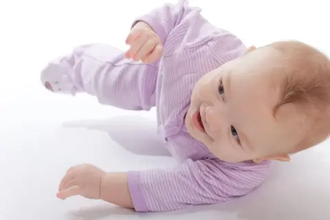 Uśmiechnięty niemowlak w fioletowym pajacyku uczy się obracać. To świetna zabawa i ważny etap rozwoju.