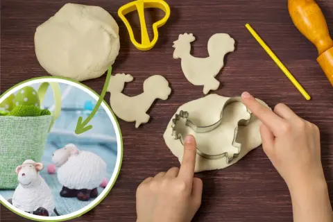 Dzieci tworzą baranka wielkanocnego diy z ciasta. Widać foremkę, wałek i pisanki.