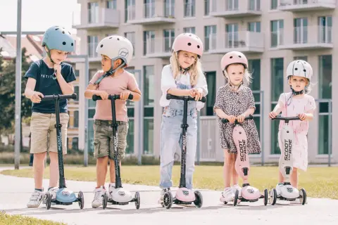 Fizjoterapeuta poleca Scoot and Ride dla dzieci. Pięcioro maluchów w kaskach na hulajnogach, gotowych do zabawy.