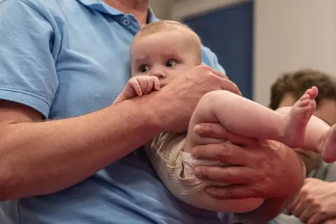 Niemowlę w ramionach mężczyzny, z odginaniem głowy do tyłu, patrzy zaciekawione.