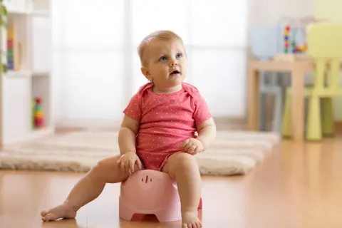 Małe dziecko w różowym body siedzi na różowym nocniku, ucząc się samodzielności.