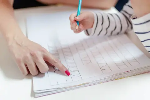Dziecko ćwiczy grafomotorykę na kartach pracy, a dorosły pokazuje mu wzory do naśladowania.