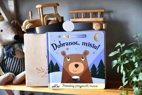 Książka "Dobranoc, misiu!" z latarką, obok pluszowego misia i drewnianych zabawek.