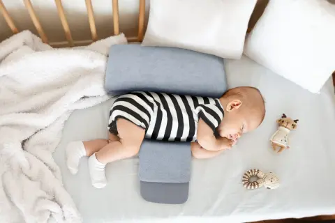Noworodek śpi na boku, podtrzymywany przez poduszkę klin. Czy poduszka klin jest bezpieczna dla noworodka? Tak, jeśli jest używana zgodnie z zaleceniami.