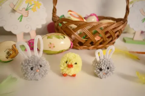 Urocze ozdoby wielkanocne zrób to sam dla dzieci: puchate króliczki i kurczaczek z pomponów, obok pisanki i koszyczek.