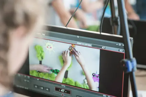 Dzieci tworzą animację poklatkową. Na ekranie widać ręce układające postacie i tło do bajki.