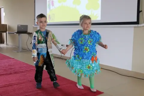 Chłopiec w eko stroju z opakowań po przekąskach i dziewczynka w sukience z kapsli i folii na pokazie mody.